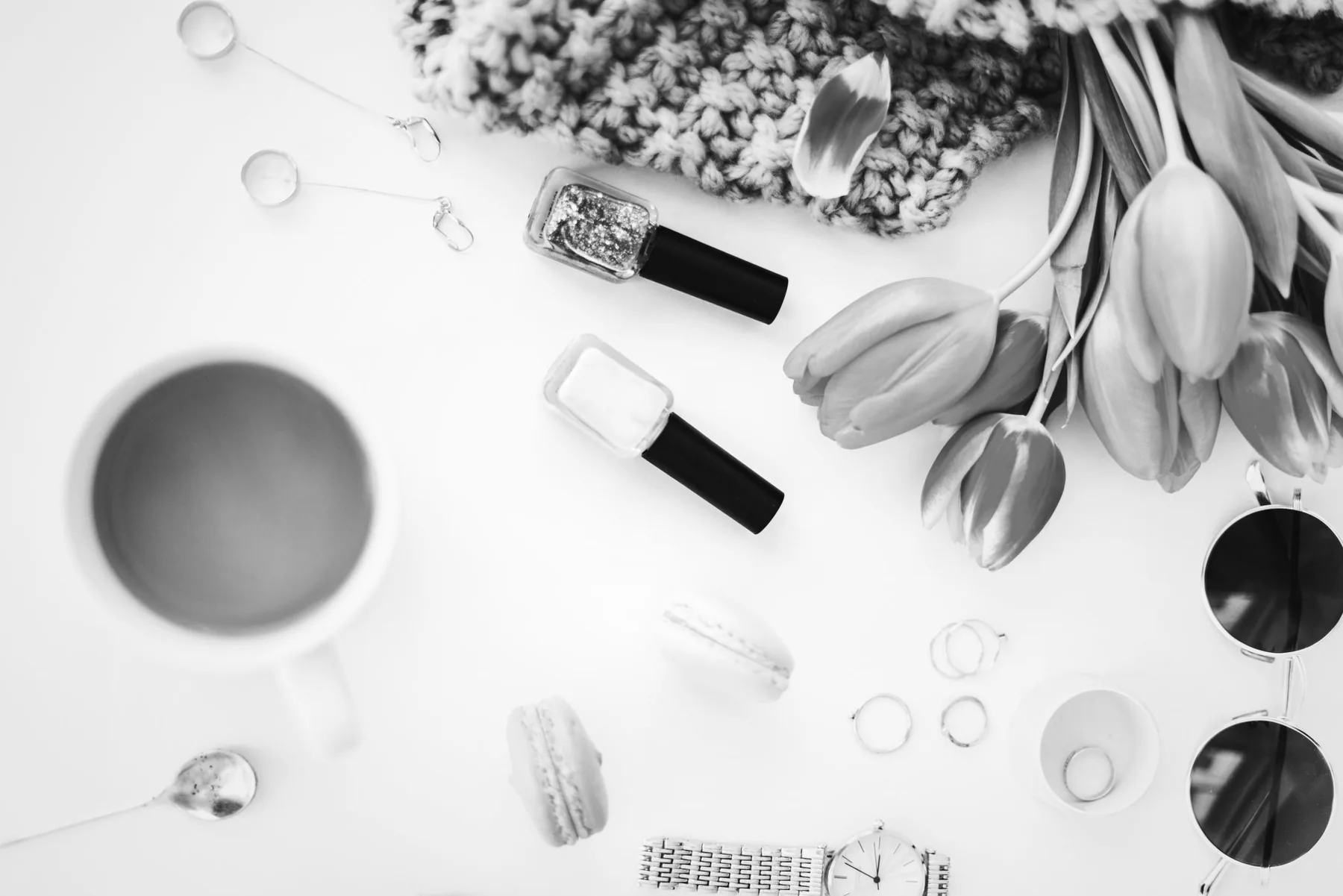 A flat lay of a coffee cup, tulips, nail polish and a watch on a white surface